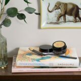 A luxurious arrangement featuring a vase of flowers, a book, and a Gold Coast Overnight Balm jar.