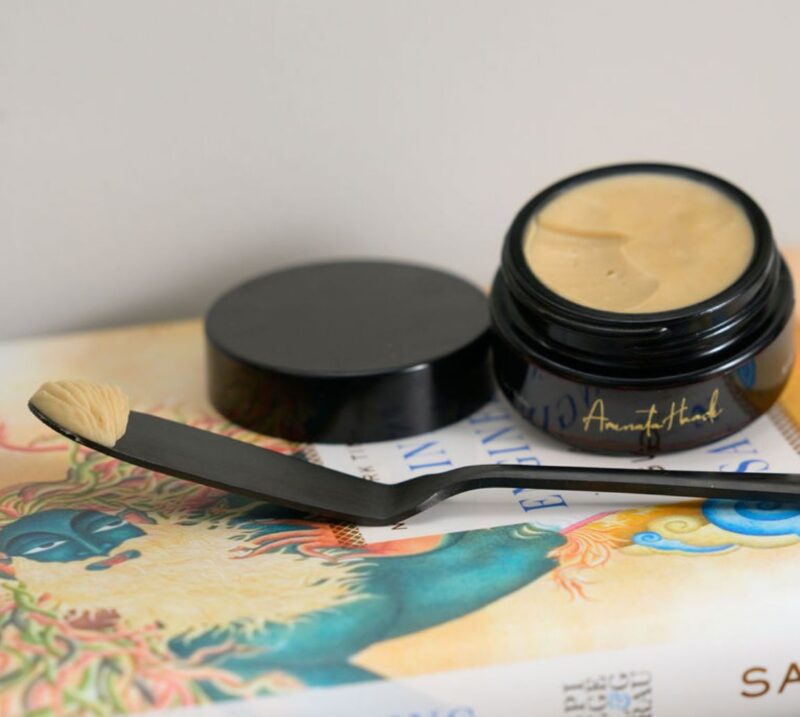 Gold Coast Overnight Balm Closeup A jar of Gold Coast Overnight Balm and a spoon elegantly placed on an open book, suggesting a moment of self-care.