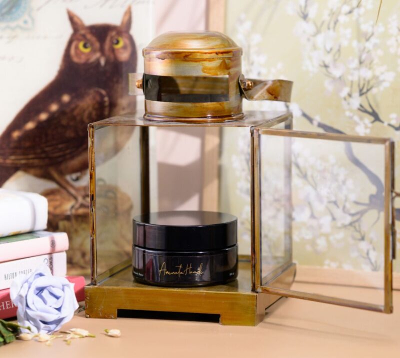A serene table setting featuring a candle, a jar of Naked Ethnobody Butter cream, and an elegant book.
