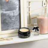 A gold shelf displays a framed picture, elegant candles, and ORI Bakuchiol Restorative Overnight Balm in a chic jar.