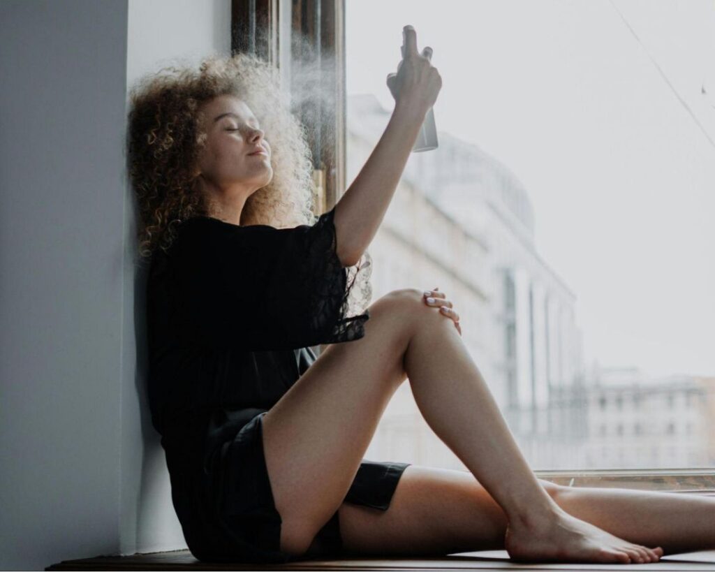 A woman sits gracefully on a window sill, legs up, embodying tranquility in a serene health and wellness setting.


