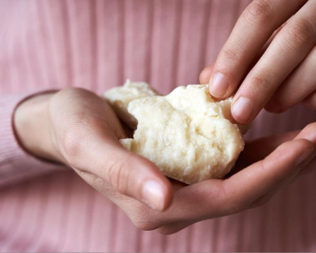 A person delicately holds a piece of shea butter, showcasing the elegance of refined or raw shea butter beside it.