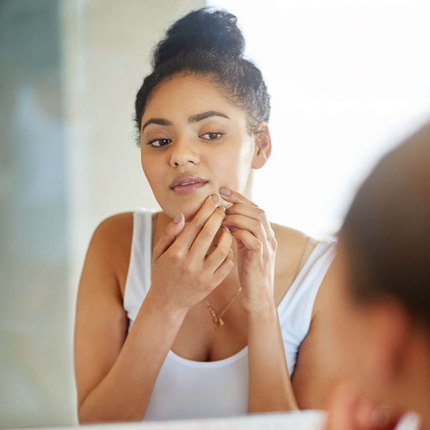 Woman with sensitive skin popping pimple in mirror.