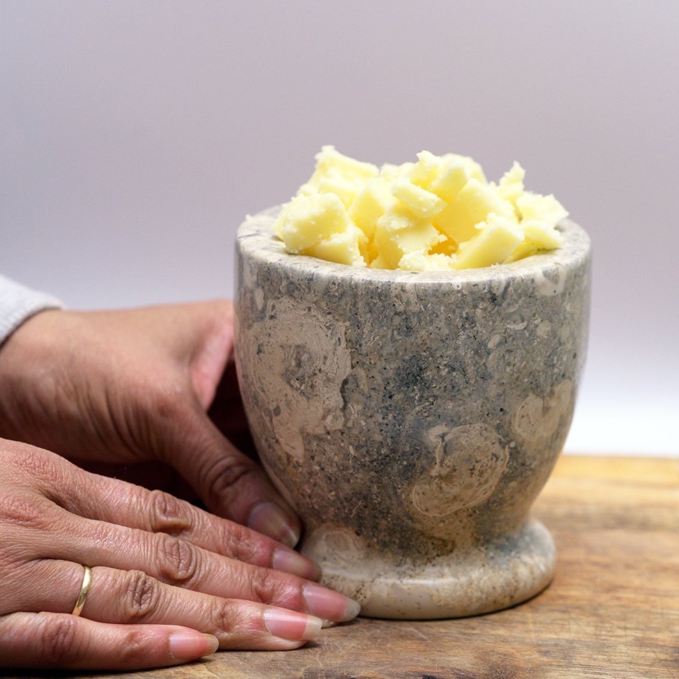 Raw shea butter in stone on mango wood cutting board. 