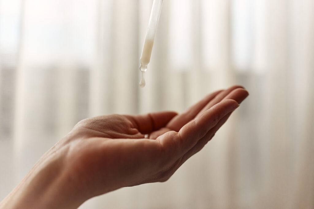 Woman applying face serum using glass pipette.