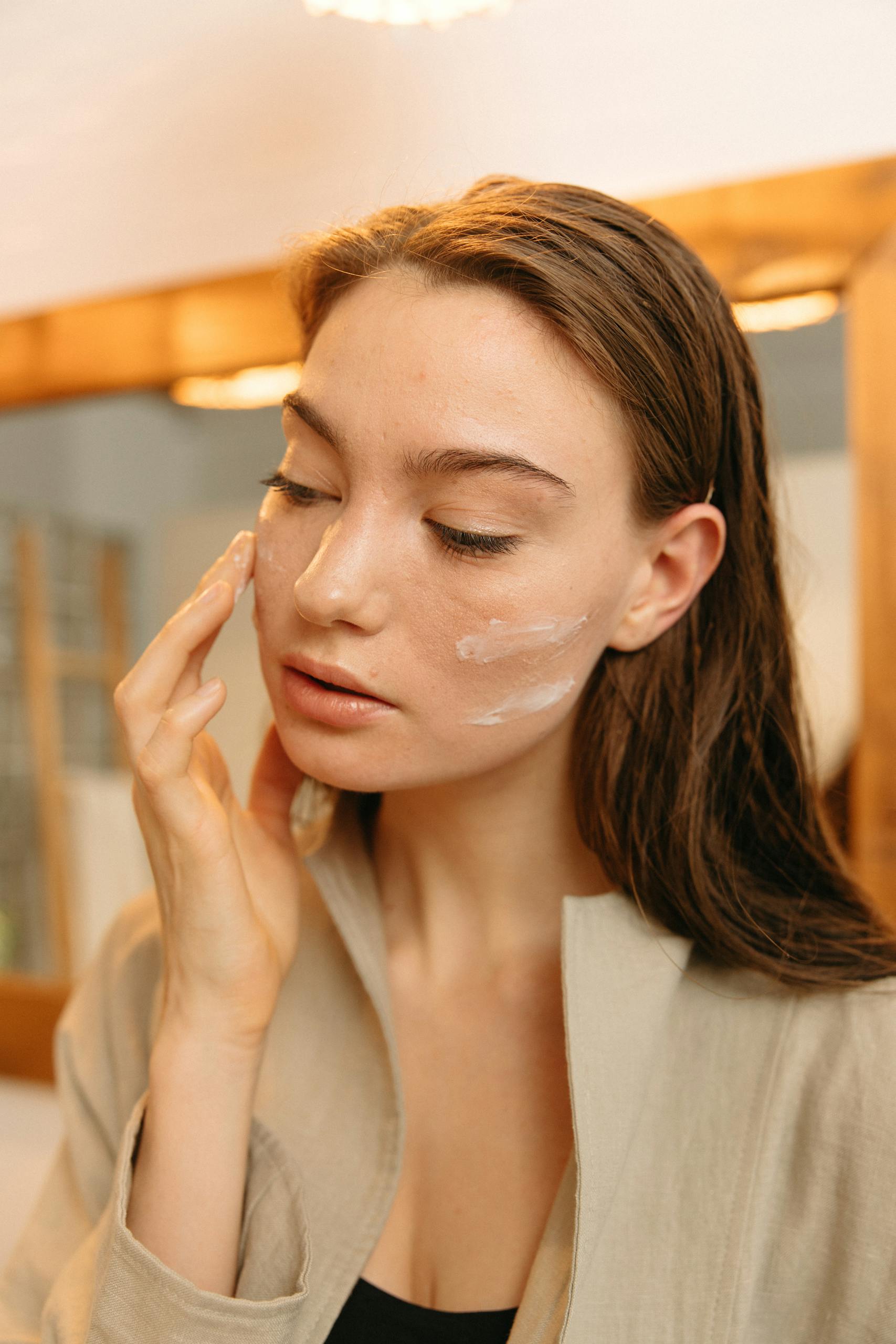 A woman gently applies skincare cream on her natural face.