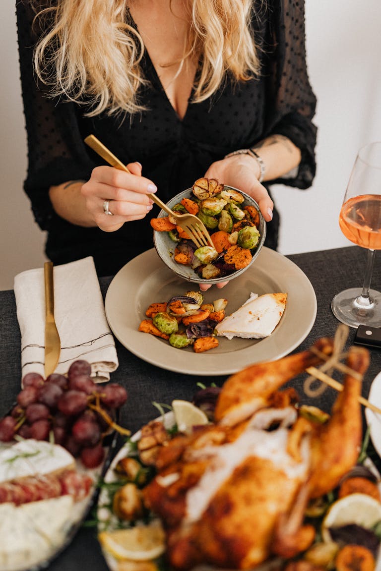 A woman serving a festive Thanksgiving meal with roast turkey, vegetables, and wine.