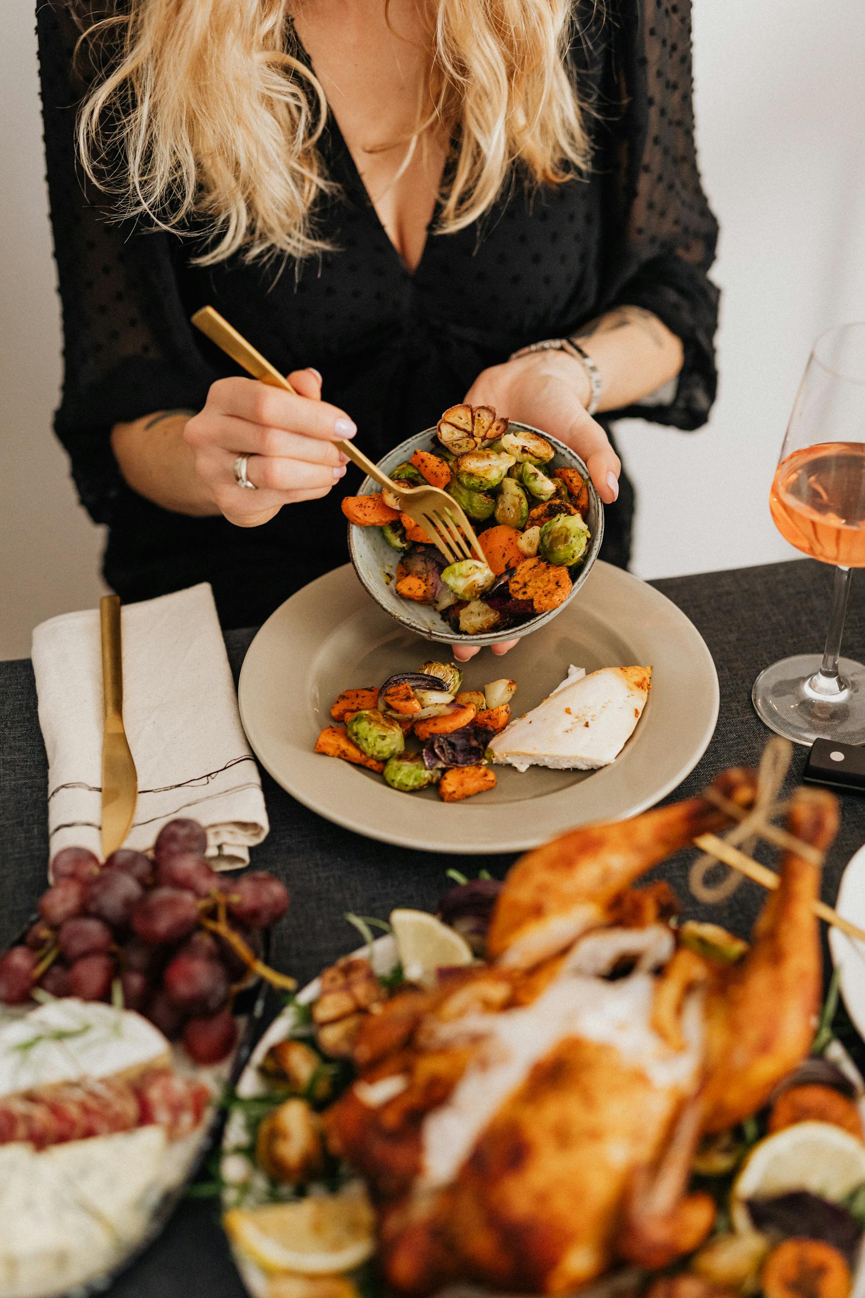 A woman serving a festive Thanksgiving meal with roast turkey, vegetables, and wine.