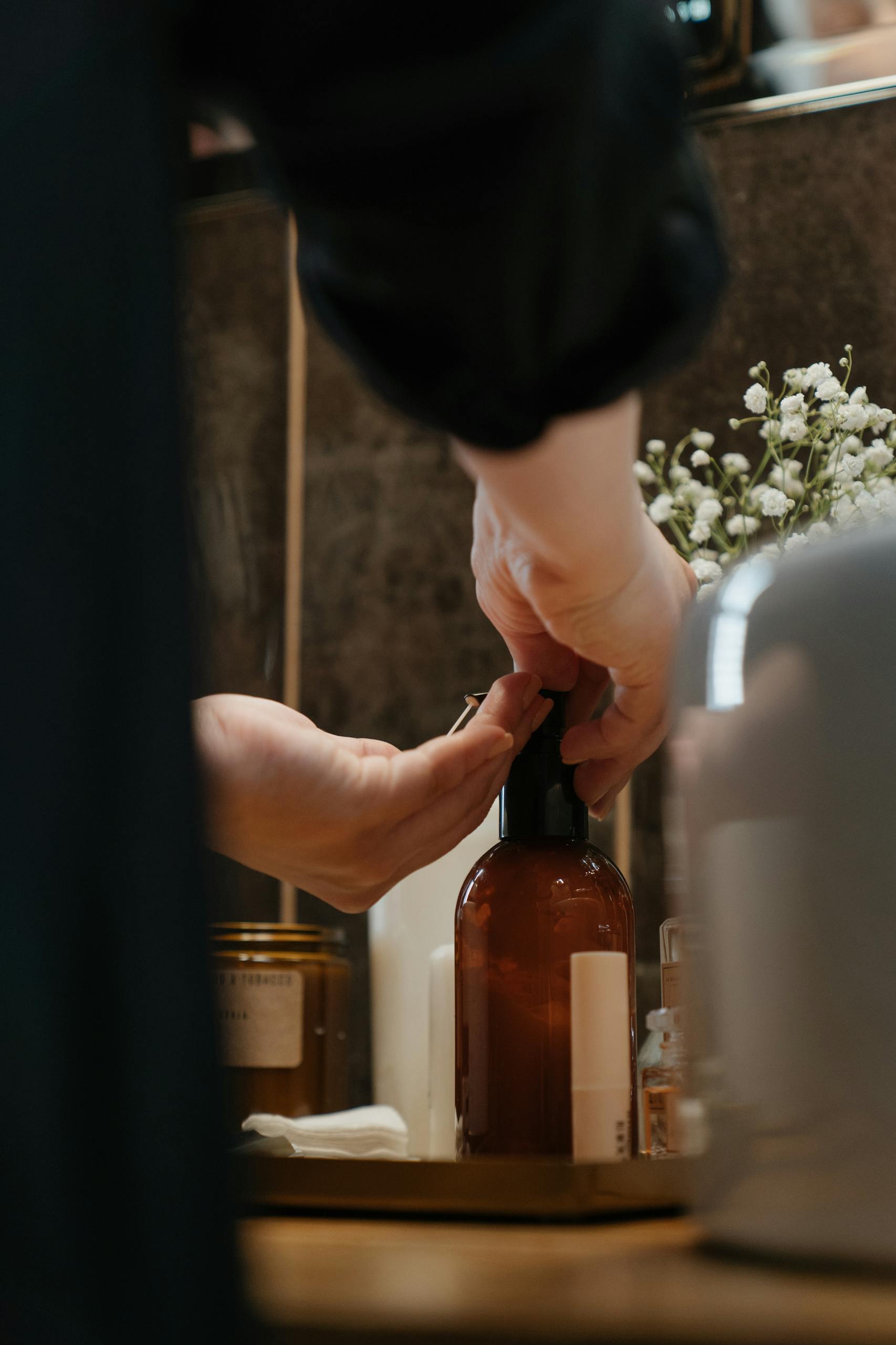 Close-up of hands using a soap dispenser in a bathroom setting, focusing on self-care and skincare.