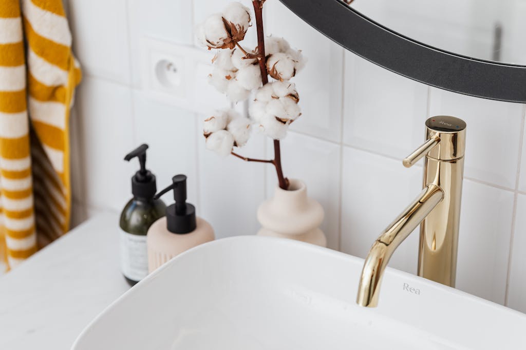 A stylish bathroom with a gold faucet, cotton plant, and modern accessories.